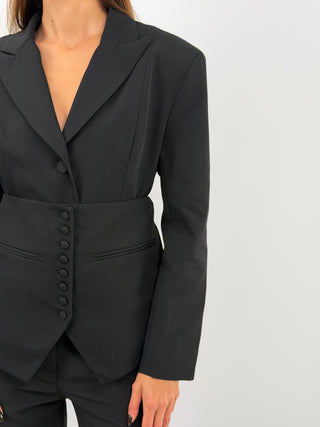 Blazer monopetto nero con collo con revers e maniche lunghe con bottoni sui polsini. Due tasche frontali decorative a filetto, spalle imbottite e fodera interna. Pannello vita coordinato regolabile e removibile tramite bottoni.