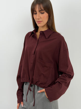 Maglia bordeaux a maniche lunghe con colletto e bottoni. Fit oversize con coulisse regolabile sul fondo e tasca frontale.