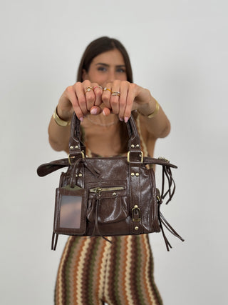 Borsa a Mano Cosmopolitan Small Marrone - Borsa marrone a mano in eco pelle con borchie decorative, manici con punto festone, tracolla regolabile e rimovibile. Tasca frontale e chiusura superiore con zip. Elegante e pratica. | Paloma Store