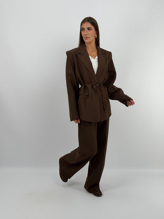 Tailleur con Spalle Strutturate Marrone - Completo tailleur marrone con blazer dalle spalle strutturate, maniche ampie, cinturina in vita e fodera interna. Pantalone a palazzo con passanti per cintura, chiusura con zip e bottone ed elastico in vita. | Paloma Store