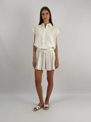 Set Camicia e Shorts con Ricamo Panna - Set coordinato panna con camicia senza maniche e pantaloncini con ricamo. Camicia ampia, più lunga sul retro, con colletto e chiusura con bottoni. Shorts con elastico in vita e lacci. | Paloma Store